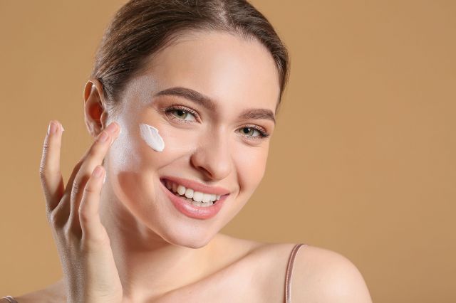 Smiling woman holds a cream, representing skin care treatment and beauty tips at Day Dream Spa, Omaha, NE.